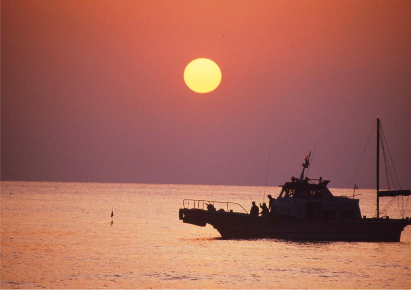 水平線に沈む夕陽と釣り船シルエット
